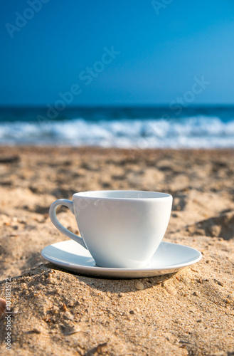white cup with tea or coffee on sand beach front of sea