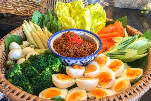 Bowl of Chili Paste with Various Type of Fresh Vegetables and Eggs in Big Rattan Basket for Traditional Thai Style Healthy Meal