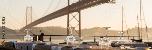 Obraz na płótnie The 25th of April Bridge in Lisbon, in front a resturant table waiting for costumers. w salonie