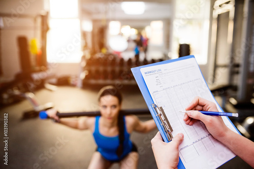 Woman exercising in gym, personal trainer, plan on clipboard photo