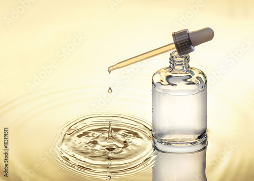 Moisturizing serum for dry skin is standing in the water,  yellow background, pipette with drop, splash.