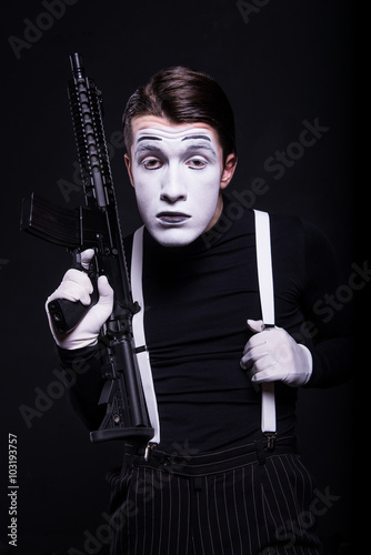 Mime with weapon/Mime in black clothes and white gloves holding rifle on black background