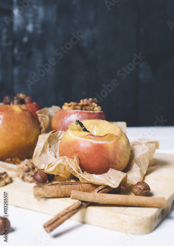 Baked apples with cinnamon sticks and hazelnuts on parchment paper and cutting board on black wooden background