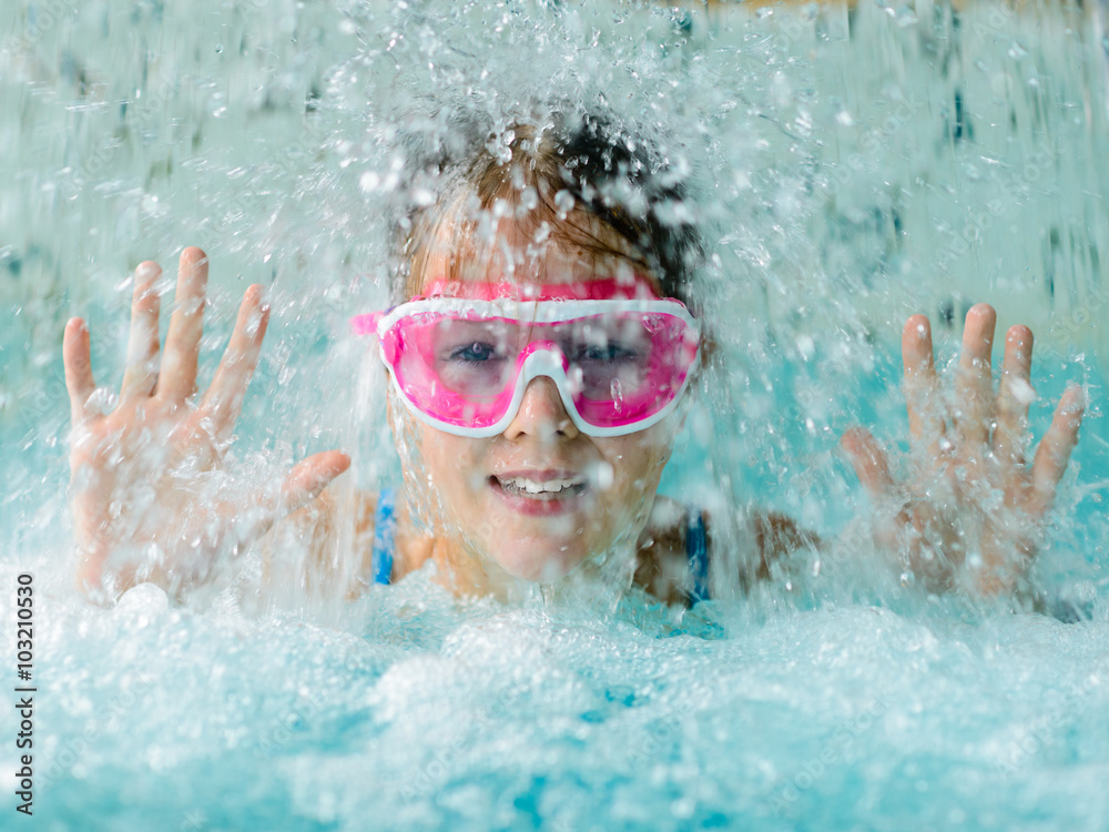 Cute happy girl in pink goggles mask in the swimming pool