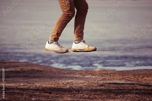 Bild auf Leinwand Man balancing on slackline with river view in the park