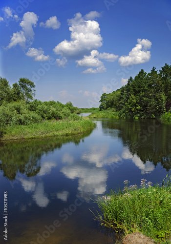 Landscape with river, forest, clouds and the reflection in the water.