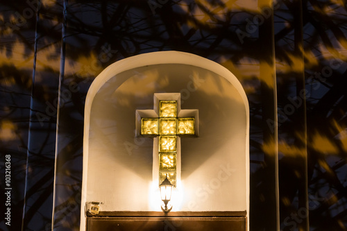 Christian Catholic cross on the facade of the church at night. Lamp above the door
 photo