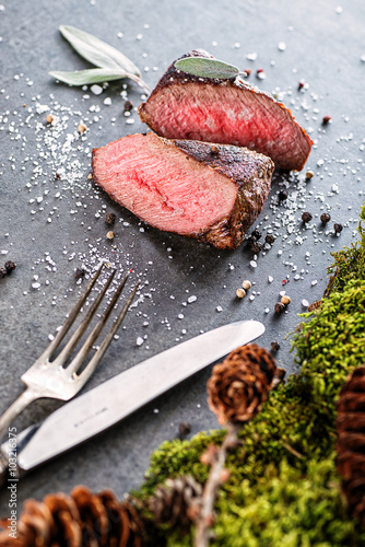 Fotografiet deer or venison steak with ingredients like sea salt, herbs and pepper and cutle