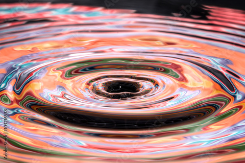 Single solitary drip drop of water into colorful reflective calm puddle pool creating ripples waves rings circles movement