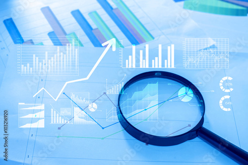 Magnifying glass and documents with analytics data lying on tabl
