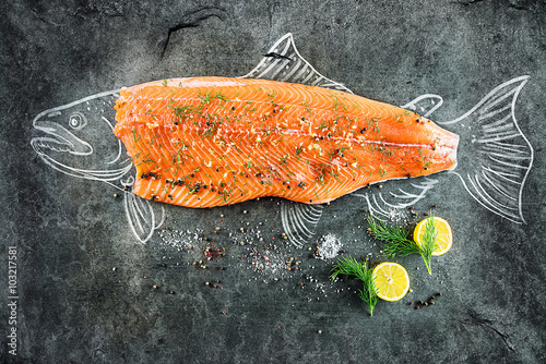 raw salmon fish steak with ingredients like lemon, pepper, sea salt and dill on black board, sketched image with chalk of salmon fish with steak