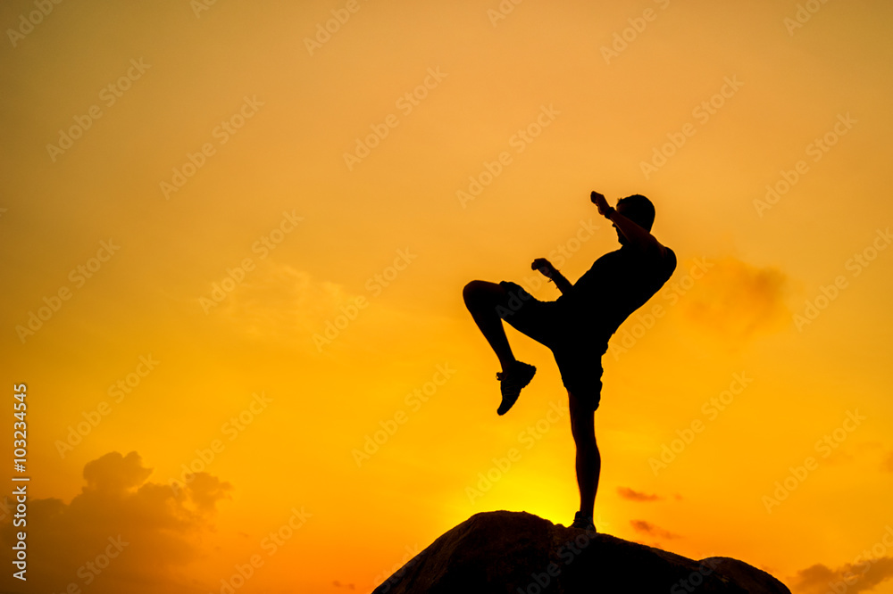 Silhouette of a man doing exercises on rocks by the sea at dawn
