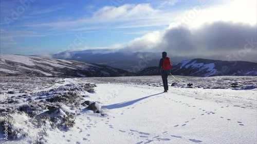 A hiker and their dog walking down from the summit of Geal Charn Mor towards Lynwilg near the Cairngorms in the Scottish Highlands in winter. photo