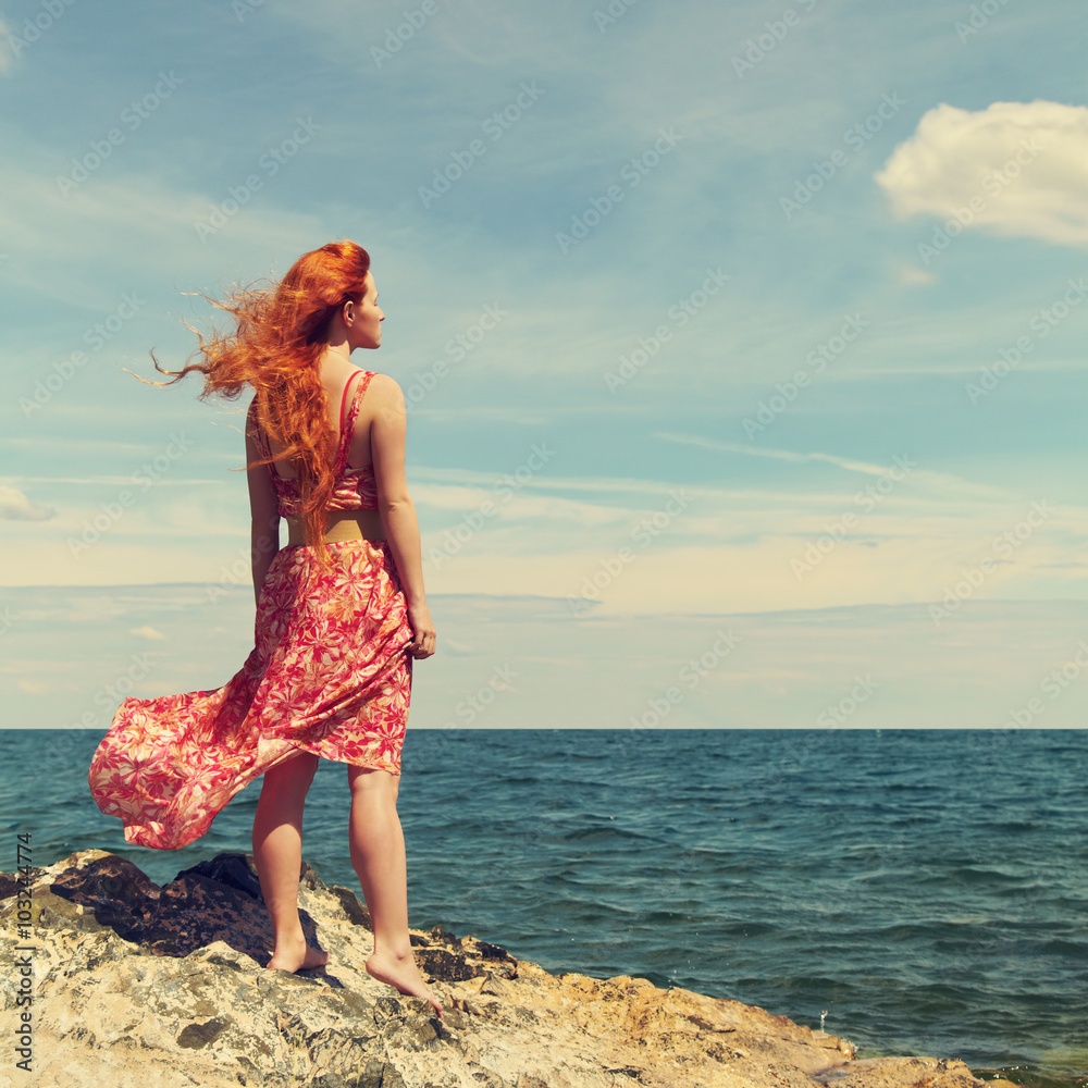 redhead young woman in a dress on the ocean coast