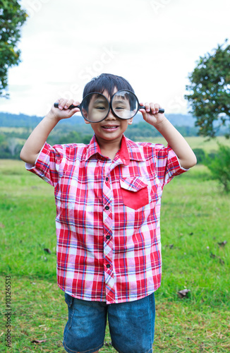 Young boy exploring nature with magnifying glass. Outdoors.