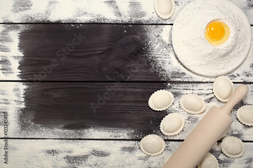 Homemade dumplings near a plate of white flour and kitchen rolling pin lying on an old rustic table. Composition for design culinary recipe or menu