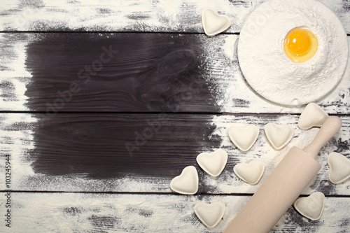Homemade dumplings near a plate of white flour and kitchen rolling pin lying on an old rustic table. Composition for design culinary recipe or menu