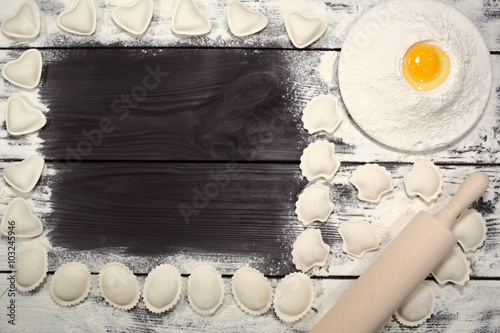 Homemade dumplings near a plate of white flour and kitchen rolling pin lying on an old rustic table. Composition for design culinary recipe or menu
