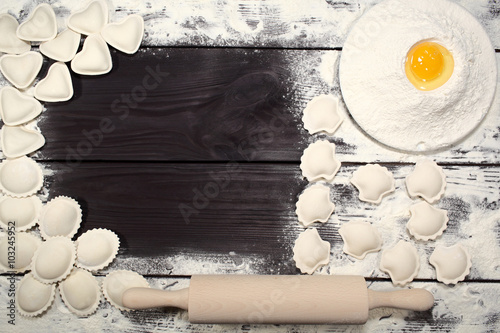 Homemade dumplings near a plate of white flour and kitchen rolling pin lying on an old rustic table. Composition for design culinary recipe or menu