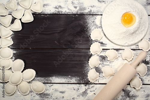 Homemade dumplings near a plate of white flour and kitchen rolling pin lying on an old rustic table. Composition for design culinary recipe or menu