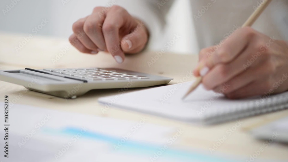 Close up of quick businesswoman's hands using a calculator and writing down notes Close up of quick businesswoman's hands using a calculator and writing down notes