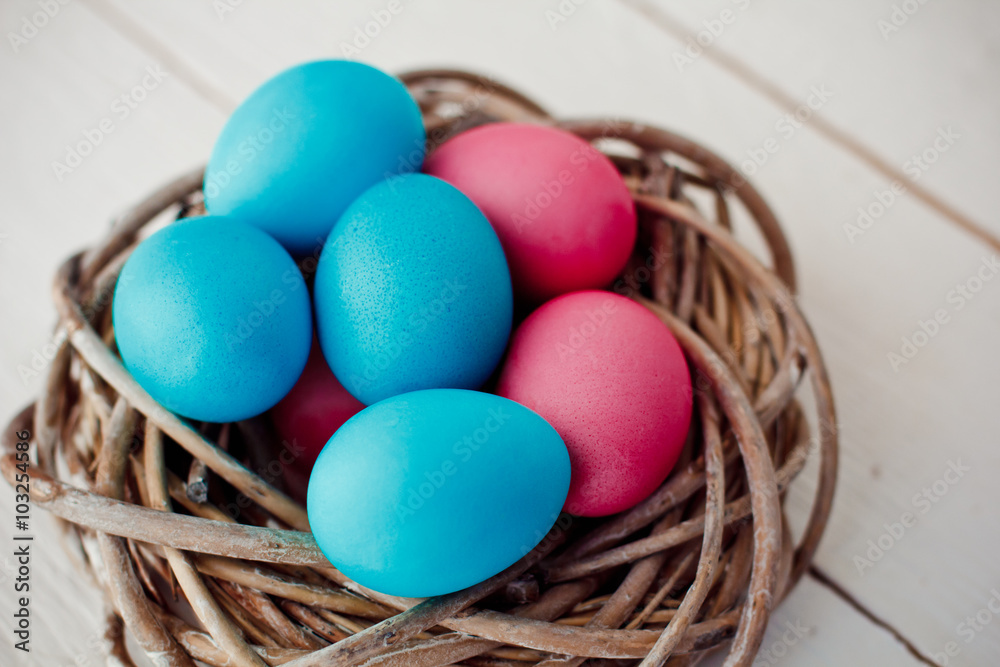blue and pink Easter eggs in nest on white wooden background blue and pink Easter eggs in nest on white wooden background