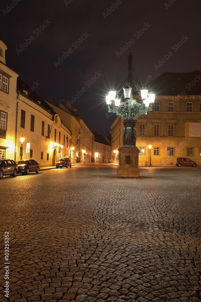 Night Picture of gas lantern or lamp on the oldest part of Prague in Hradcany, Prague castle. Lantern and the statue under is example of art deco style in prague, street is covered by old stone cubes.