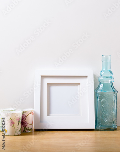 A small white picture frame with white inlay sitting on a wooden desk. The background is white and the foreground desk is soft pine wood.