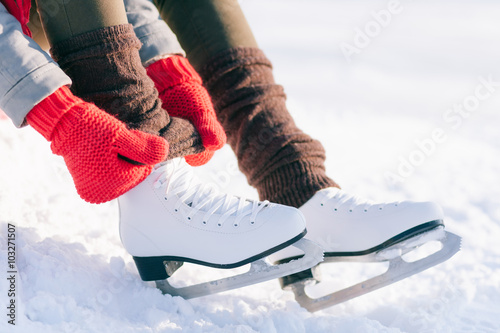 Girl in dress skates mittens tying shoelaces