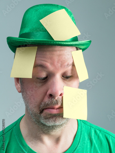 Photograph of a man in St. Patrick's Day reveling attire, with a Leprechuan hat and green shirt. His face and hat are covered in yellow sticky reminder notes. photo