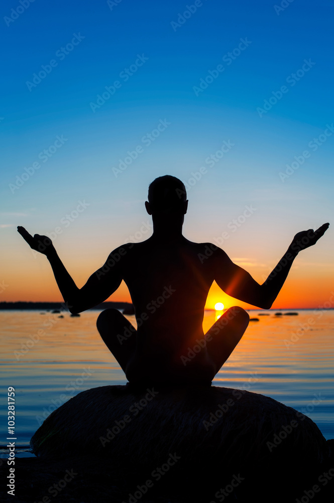 Meditating man silhouette on multicolored sunset background.