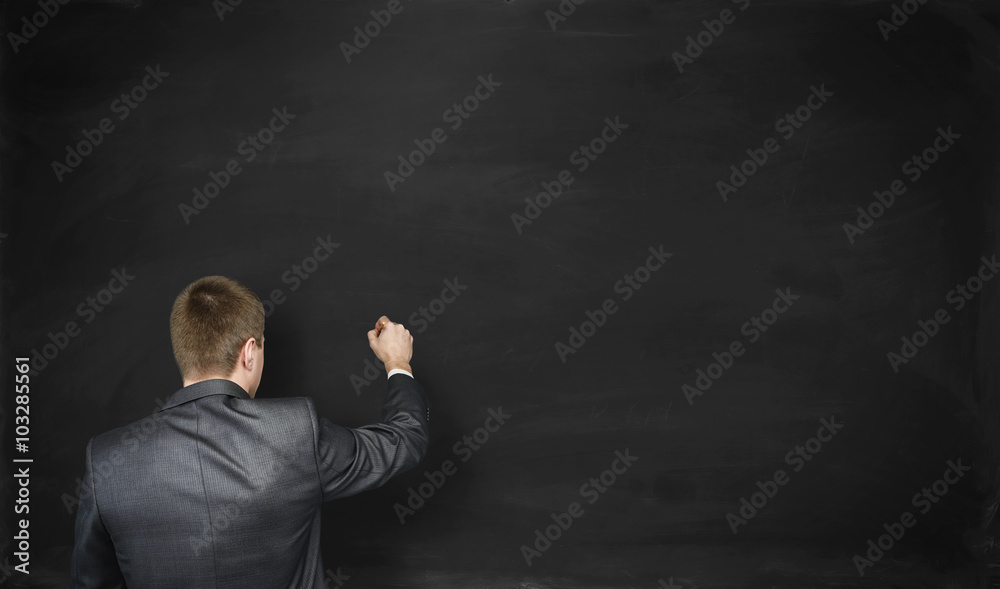 Back view businessman going to write something on a empty black wall Back view businessman going to write something on a empty black wall