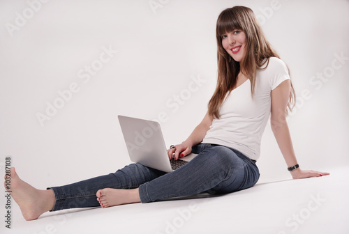 Eine junge Frau, Mädchen sitzt barfuß auf dem Boden und hat einen Laptop vor sich.