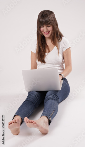 Eine junge Frau, Mädchen sitzt barfuß auf dem Boden und hat einen Laptop vor sich.