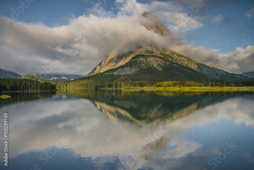 Clouds and early morning sunlight on Grinnell Point with beautiful reflections in Swiftcurrent Lake, Glacier National Park, USA photo