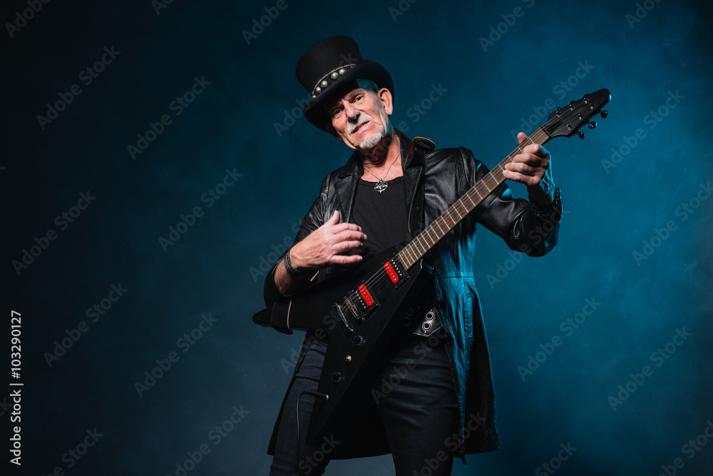 Fototapeta premium Heavy metal senior man with electric guitar in front of dark blu
