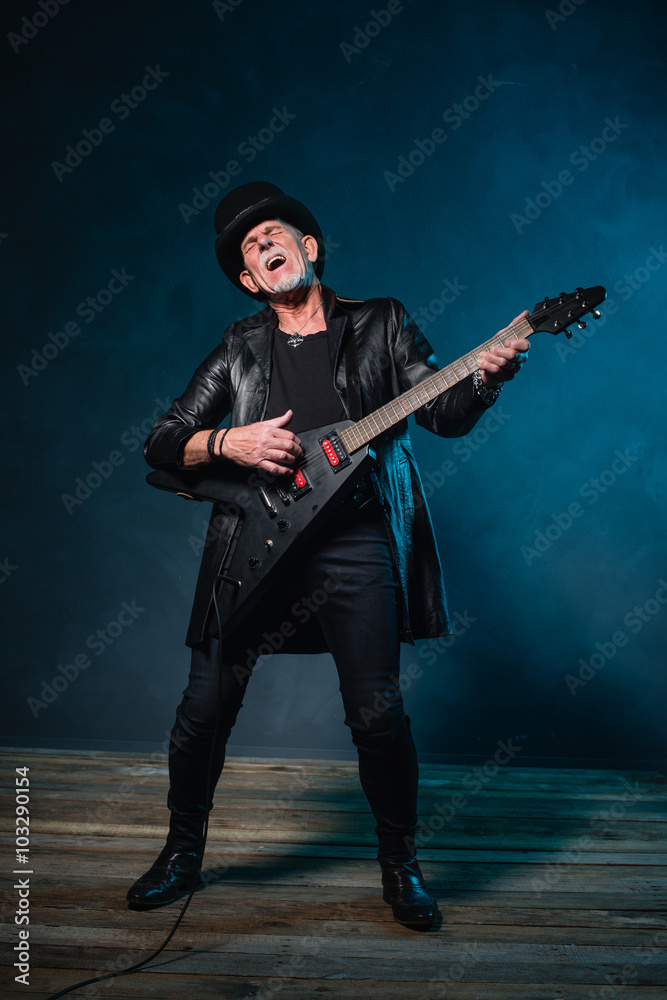 Fototapeta premium Heavy metal senior man with electric guitar in front of dark blu