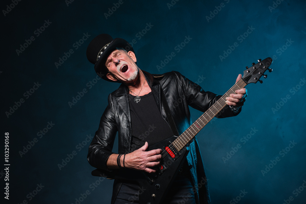 Fototapeta premium Heavy metal senior man with electric guitar in front of dark blu