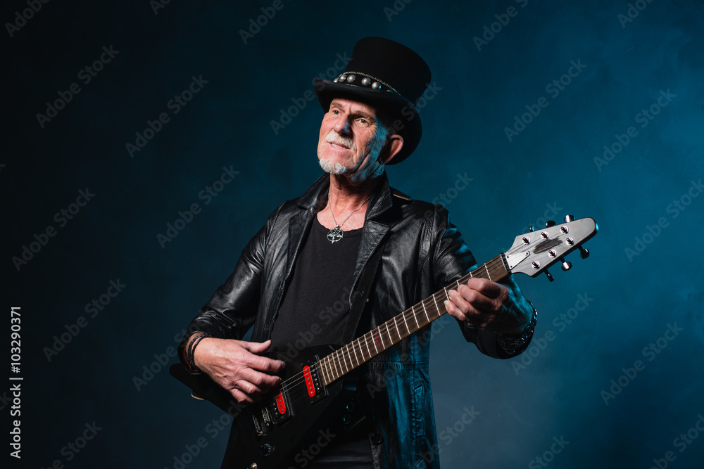 Fototapeta premium Heavy metal senior man with electric guitar in front of dark blu