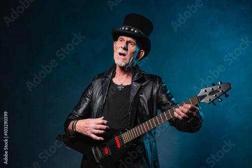 Heavy metal senior man with electric guitar in front of dark blu