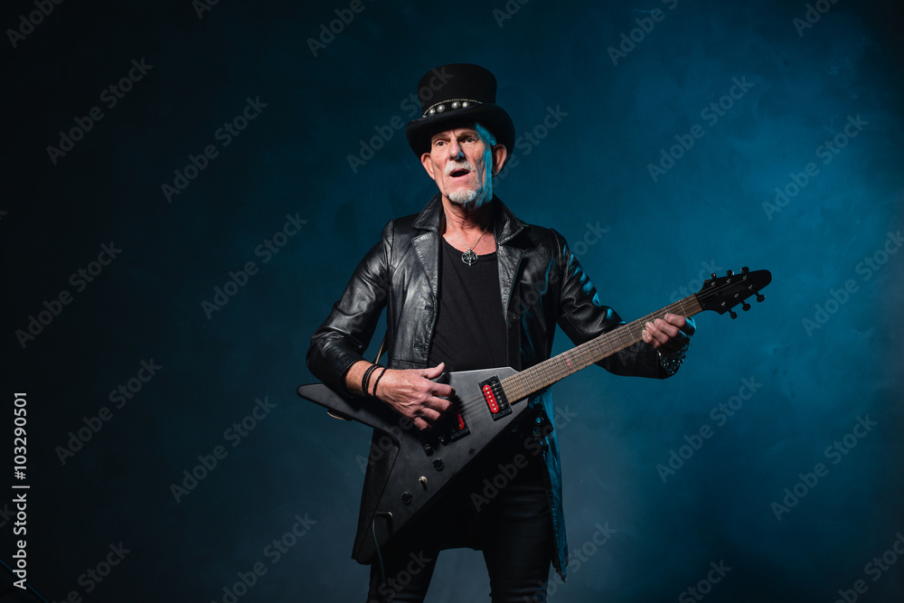 Heavy metal senior man with electric guitar in front of dark blu Heavy metal senior man with electric guitar in front of dark blu