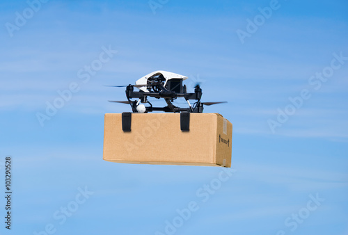 Slika na platnu Drone flying through the air with a delivery box pakage clamped on to deliver to