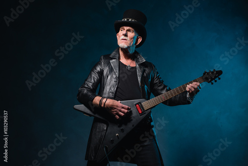 Heavy metal senior man with electric guitar in front of dark blu
