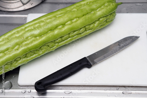 Fresh green bitter melon or bitter gourd on chopping board with knife