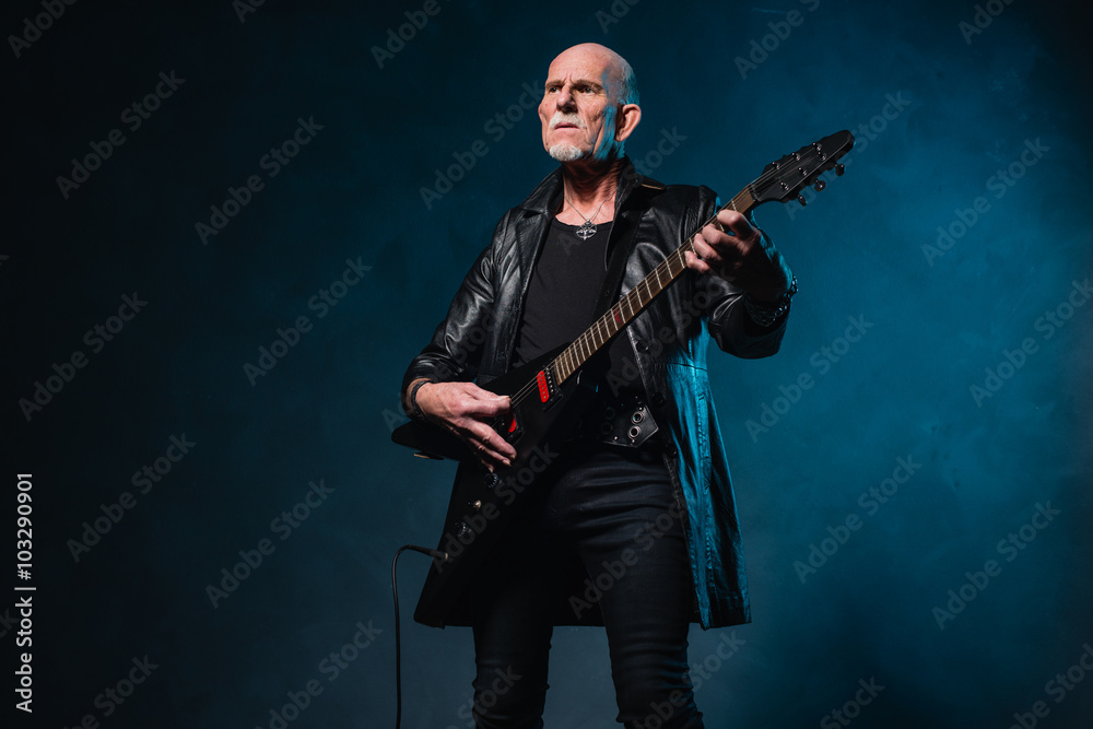 Bald heavy metal senior man with electric guitar in front of dar Bald heavy metal senior man with electric guitar in front of dar