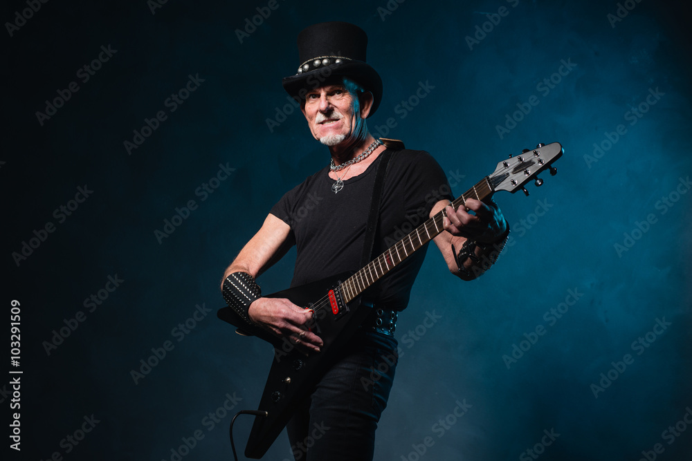 Heavy metal senior man with electric guitar in front of dark blu