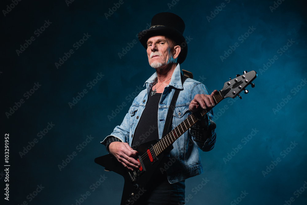 Heavy metal senior man with electric guitar in front of dark blu
