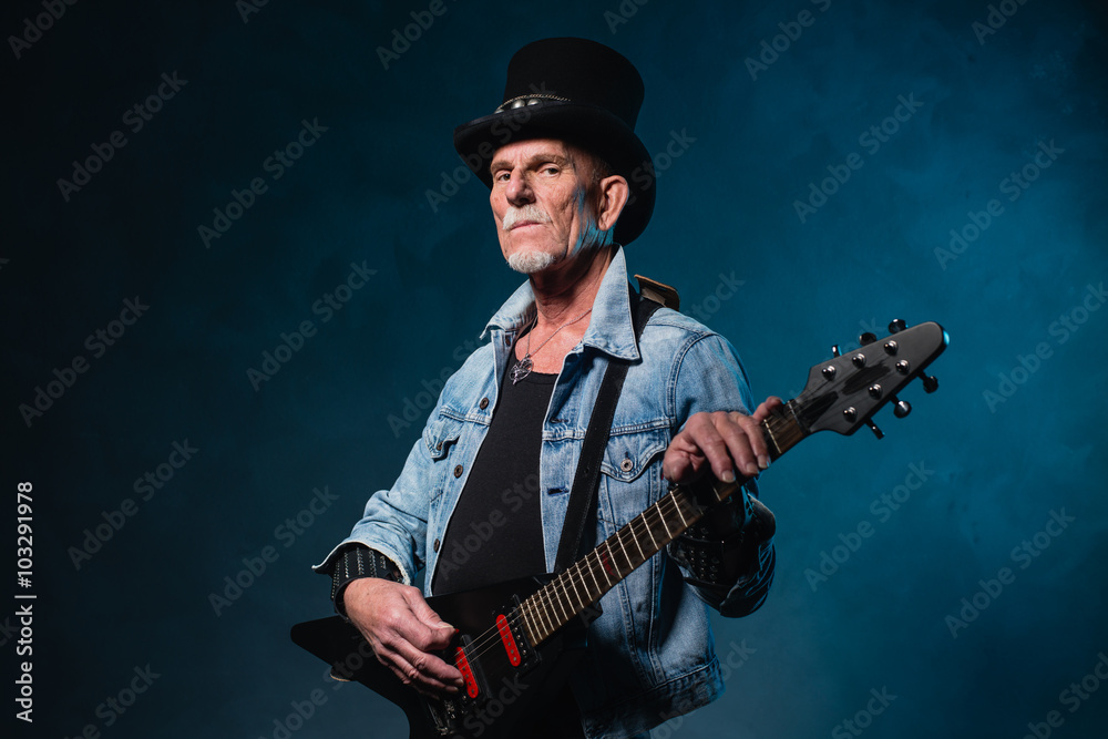 Heavy metal senior man with electric guitar in front of dark blu Heavy metal senior man with electric guitar in front of dark blu