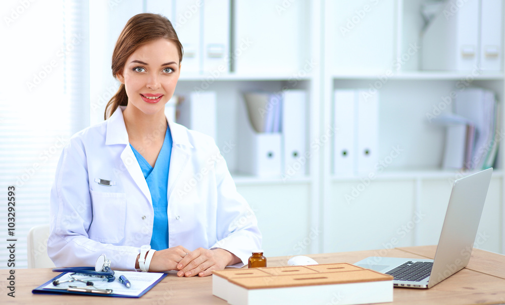 Beautiful young smiling female doctor sitting at the desk and writing. Beautiful young smiling female doctor sitting at the desk and writing.