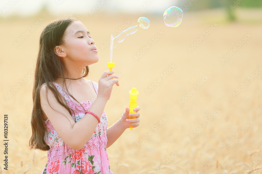 child girl blowing soap bubbles at sunset